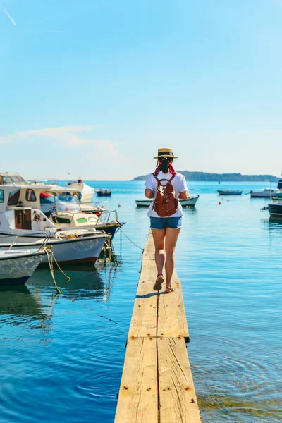 年轻漂亮的女人在海湾的木制码头旅行 背景的船只 — 图库照片