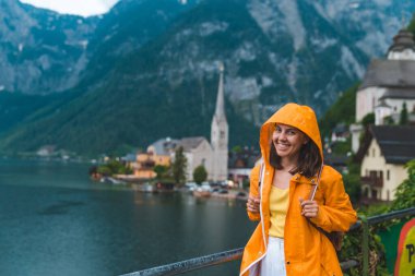 Sarı yağmurluklu kadın Hallstatt City panoramik manzarasına bakıyor