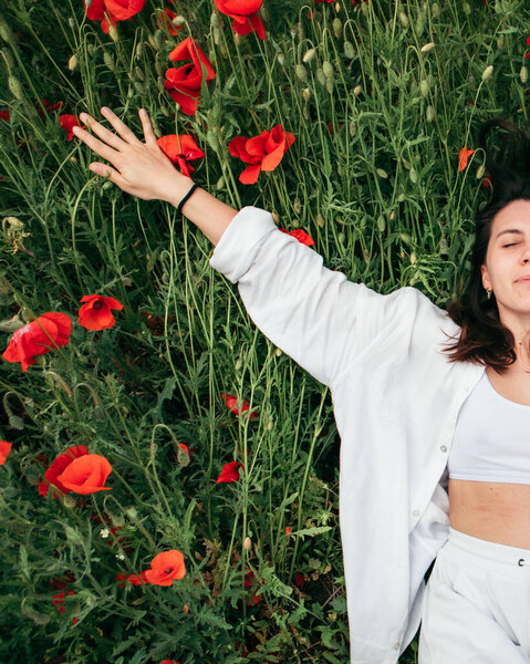 young pretty woman laying down at the field of poppy flowers. copy space. summer time