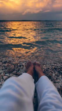 Sahilde uzanmış denizin üstünde gün batımını seyreden bir kadın. vücut parçaları bacaklar