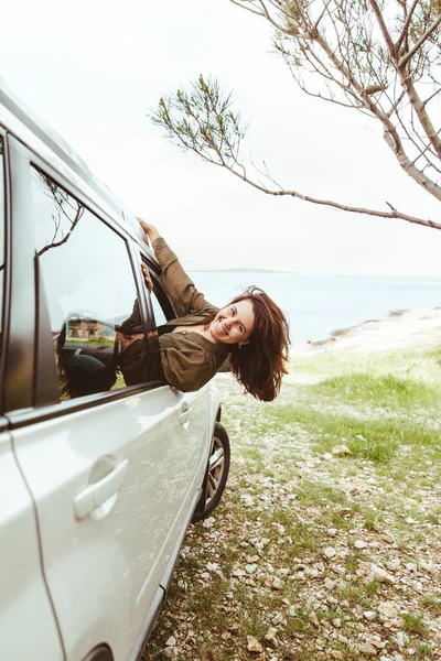 young pretty woman stick out from car window sea beach on background . summer vacation