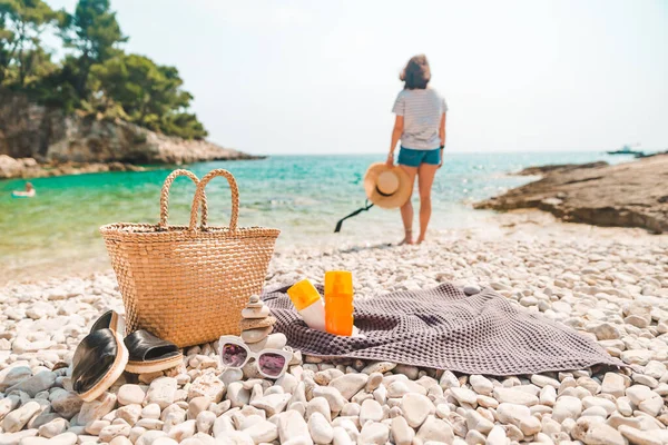 海滨女子背景下的沙滩草帽和装有拖鞋和防晒霜的沙袋 — 图库照片
