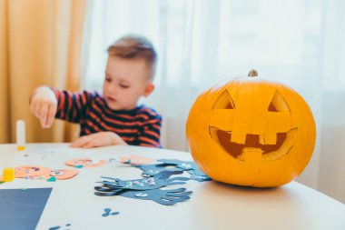 Balkabağı kafalı küçük çocuk cadılar bayramı hazırlığı yapıyor.