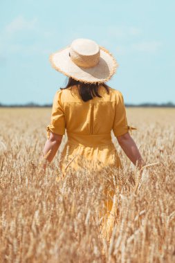 Sarı elbiseli kadın buğday tarlasında yürüyor. yaz zamanı