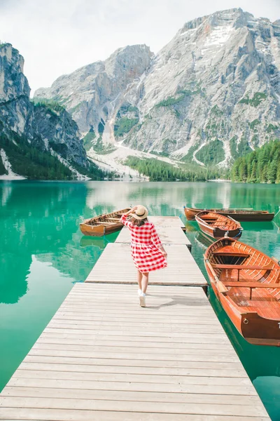 Mladá hezká žena červené šaty procházky po dřevěném molu s čluny. letní dovolená — Stock fotografie