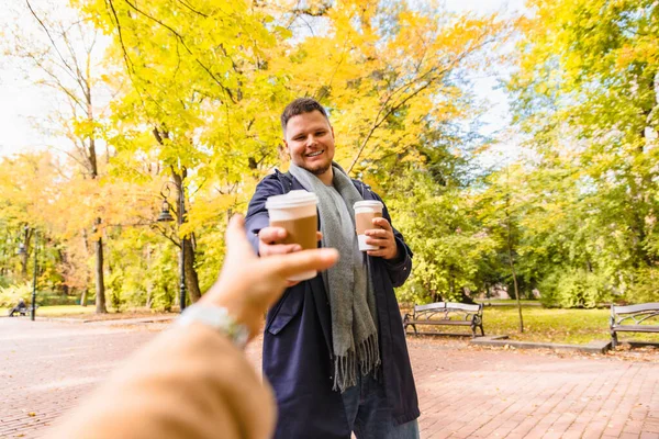 Man brings coffee to friend drink to go outdoors autumn city park — Stock Photo, Image