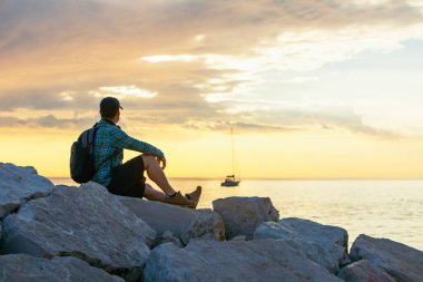 Sırt çantalı bir adam gün batımını seyrediyor. Boşluğu kopyala