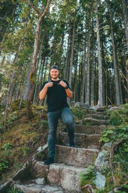 Sırt çantalı siyah elbiseli, ormanda yürüyüş yapan güçlü bir adam.