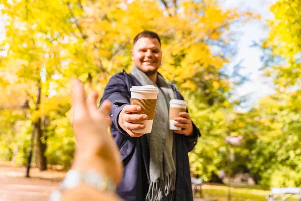 man brings coffee to friend drink to go outdoors autumn city park lifestyle