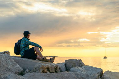 Sırt çantalı bir adam gün batımını seyrediyor ve müzik dinliyor. Boşluğu kopyala