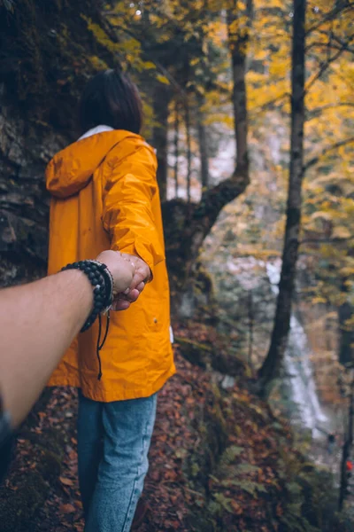 黄色のレインコートを着た女性がトレイルを歩いて森の滝の季節に行き — ストック写真