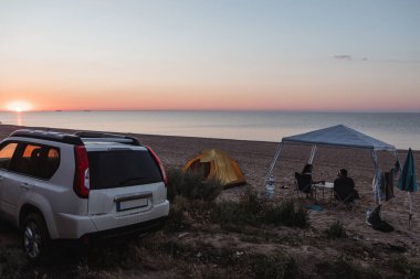 Kumsaldaki kamp alanında. İnsanlar gün batımını seyrediyor. Yaz seyahati