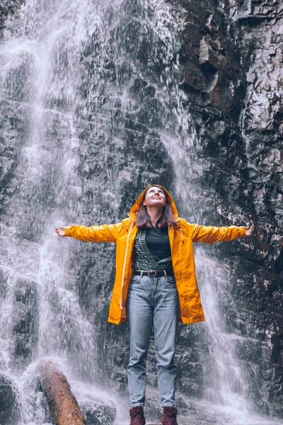 woman in yellow raincoat at autumn waterfall hiking concept