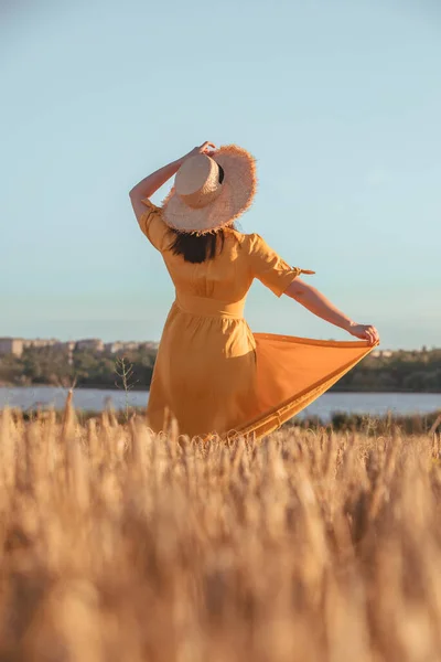 woman in yellow sundress walking by wheat field. summer time