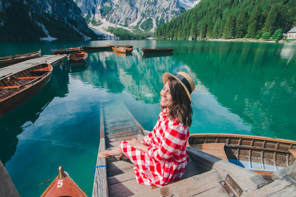 woman in red sundress sitting on wooden stairs looking at lake in mountains. summer vacation