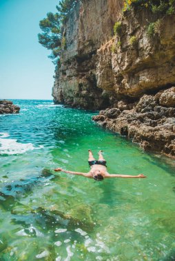 Genç adam yazın kayalıkların arasında, körfezde yüzüyor. Kopya uzay.