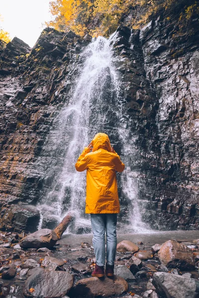 woman in yellow raincoat at autumn waterfall hiking concept