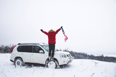 Tepenin tepesinde elinde ABD bayrağı olan bir adam arazi aracının yanında güzel bir kış manzarası arıyor. özgürlük kavramı