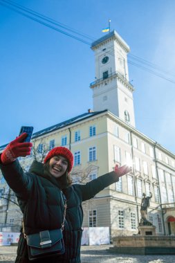Kadın, arka plandaki şehir seyahati konseptiyle ilgili Lviv Belediye Sarayı 'nda selfie çekiyor. Boşluğu kopyala