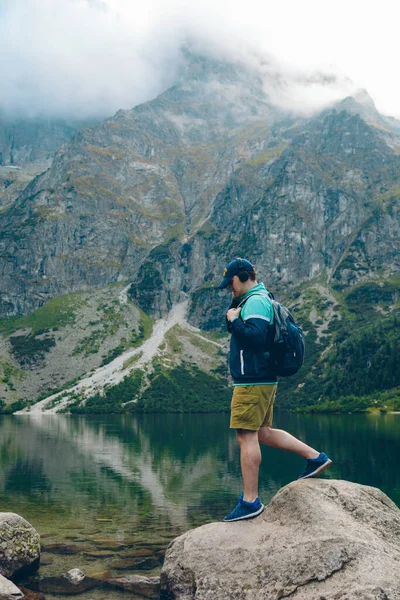 man listening music in headset while hiking around lake in mountains copy space