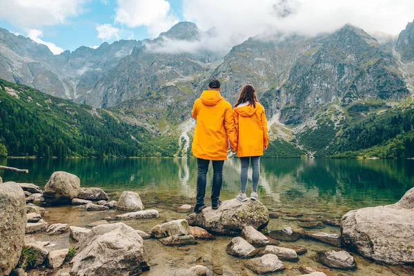 Hombre con mujer en impermeable amarillo en el soleado día de otoño mirando el lago en las montañas de Tatra — Foto de Stock