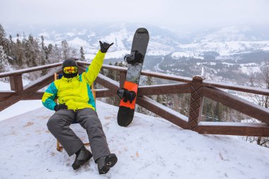 Adam sandalyede oturmuş, karlı dağların panoramik manzarasına bakıyor. kış snowboard konsepti