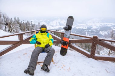 Adam sandalyede oturmuş, karlı dağların panoramik manzarasına bakıyor. kış snowboard konsepti