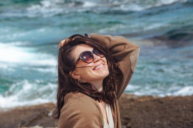 Deniz kıyısında doğanın gücünün tadını çıkaran bir kadın. Rüzgarlı bir hava. Yaz tatili. arkaplandaki dalgalar