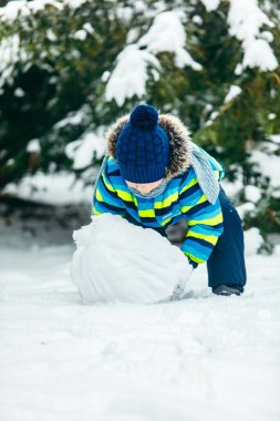 Küçük tatlı çocuk kardan adam yapıyor. Yuvarlanan büyük bir kartopu. kış tatili