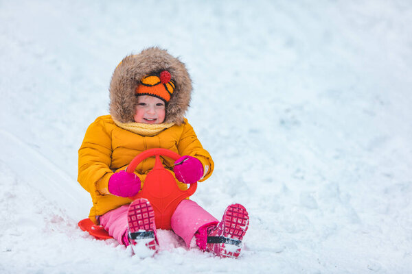 little kid at sledge sliding down by winter snowed hill