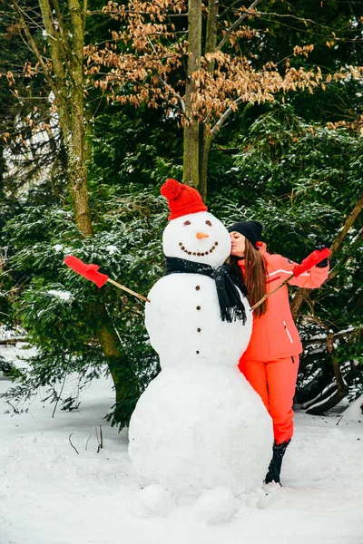 Kırmızı şapkalı ve eldivenli kardan adamla poz veren kadın. Kış tatili