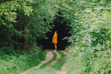 Sarı yağmurluklu adam, ormanın karanlık girişinin önünde zımparalıyor. Boşluğu kopyala