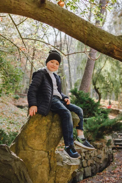 Sonbahar Şehir Parkı 'ndaki kayanın üzerinde oturan küçük çocuk. Fotoğraf için poz vermek. Doğa