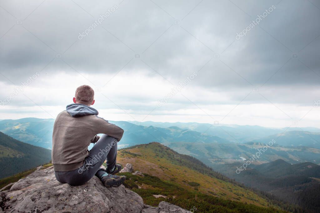 young strong man sitting on the rock at the top of the mountains peak enjoying the view. hiking concept