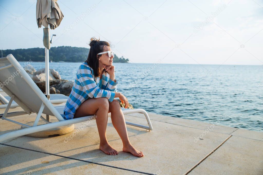 young pretty woman sitting on sun lounger looking at sunset over the sea