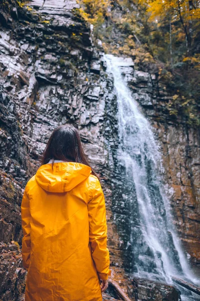 Жінка в жовтому плащі на осінньому водоспаді — стокове фото