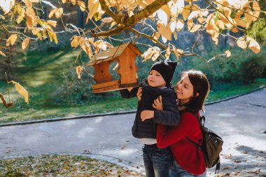 Küçük çocuklu genç anne kuş yemliğine tohum koydu. sonbahar sezonu