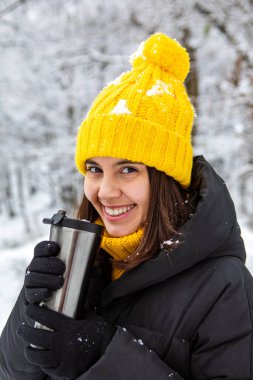 Kış kıyafetli gülümseyen kadın doldurulabilir kupa fotokopi alanından sıcak bir şeyler içiyor.