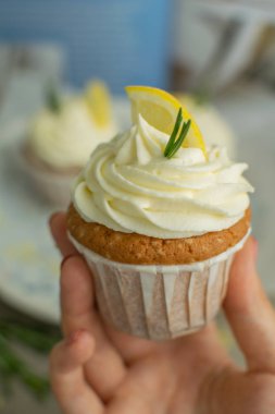 Peynir kreması ile elinde tatlılar güzel ev yapımı lezzetli tatlı limon cupcake yeme, lor, limon dilim, keten masa örtüsü mavi yemek kitabı arka plan biberiye dalı, seçici odak, yakın çekim, kopya alanı, bokeh, bulanık geri 