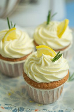 Peynir kreması ile lezzetli güzel tatlı limon cupcakes, limon dilimi, parchament arka plan ile coloreful plaka biberiye ile süslenmiş, seçici odak, yakın çekim, yerden kopya alan, üstten.