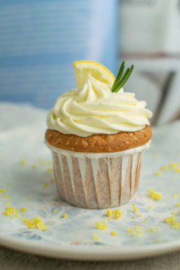 Peynir kreması ile perchament ile mavi boyalı plaka üzerinde bir Hafif limon cupcake, lor, limon dilim, biberiye ve lezzet mavi tarifi kitap arka plan, seçici yumuşak odak, yakın, kopya alanı ile süslenmiş.
