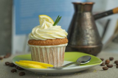 Fırında tatlı limoncupcake ve cezve kahve, kaşık ve kavrulmuş kahve çekirdekleri, peynir kreması, limon dilimi, keten masa arka planda biberiye dalı ile tabak