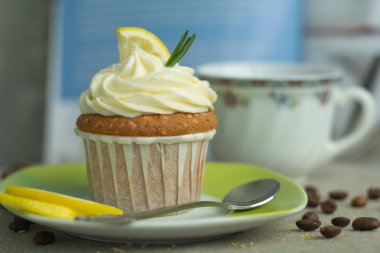 Kahve zaman fincan, kavrulmuş fasulye ve peynir kremaile tatlı tatlı limon cupcake, limon, keten masa örtüsü mavi arka planda biberiye, seçici odak, yakın çekim, yerden kopya alan, üstten.