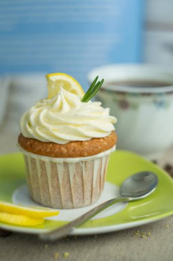 Kahve bulanık desen fincan, krem peynir, limon, keten masa örtüsü mavi arka planda biberiye, yumuşak odak, yakın, kopya alanı, yeşil tabak ve kaşık ile tatlı limon cupcake