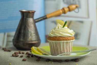 Kaşıkla yeşil tabakta tatlı taze ev yapımı pasta limon cupcakes ile kavrulmuş kahve çekirdekleri, peynir kreması ile, limon dilim, keten masa örtüsü mavi yemek kitabı arka planda biberiye dalı, arka da cezve ile, metin ile seçici yumuşak odak