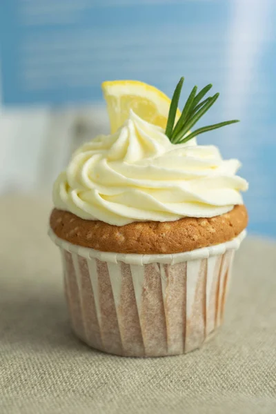 Homemade lemon cupcakes with cream cheese, slice of lemon, bundle of rosemary at blue background at linen tablecloth, selective focus, close up, copy space, from the top.