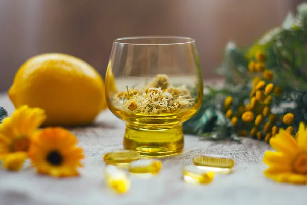 Geleneksel tıp geçmişi, cam bardakta kurumuş papatya çiçekleri, çuval bezinde bulanık limon, omega 3 kapsülü, tansi, masada takvim.