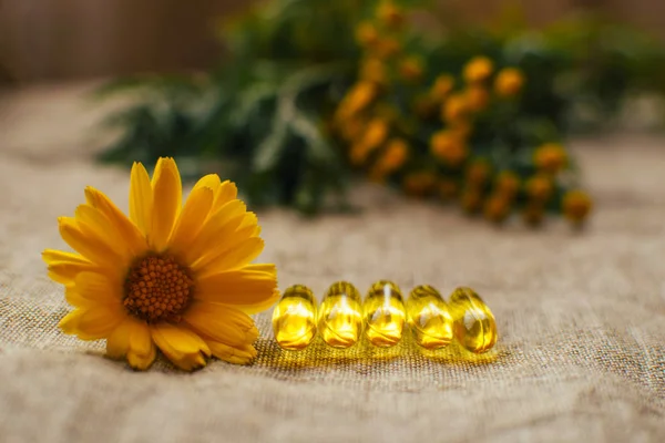 Balık yağı kapsüllerini ve takvim çiçeklerini kapatın. Masadaki keten kumaşın arka planında tansi olsun. Kopyalama alanı, yumuşak odak noktası.