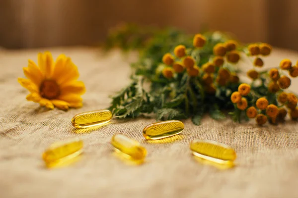 Fermer les capsules d'huile de poisson avec fleur de calendula et tanaisie à l'arrière-plan sur le tissu de lin à la table, espace de copie, mise au point douce — Photo