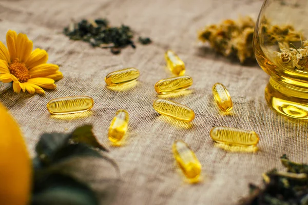 Balık yağı kapsülleri, bitkiler, cam bardak, takvim, cam bardak, masa örtüsü üzerinde ahududu yaprağı, yumuşak odaklı alternatif tıp düzeni.